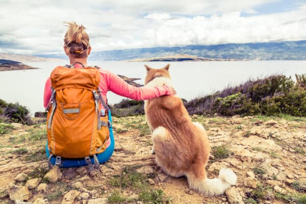 Woman and dog sit on cliff overlooking ocean.